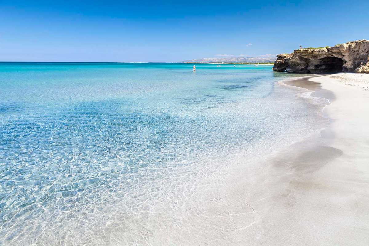 Panorama aereo delle spiagge sabbiose di Peschici, mare cristallino, lidi attrezzati e famiglie con bambini. Inquadratura ampia con il paesino sullo sfondo.