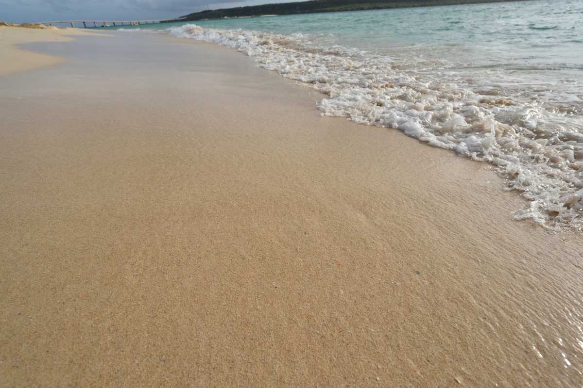 Famiglie in relax su una spiaggia sabbiosa di Peschici, bambini che giocano vicino all’acqua, cabine colorate e ombrelloni. Atmosfera estiva, cielo sereno.